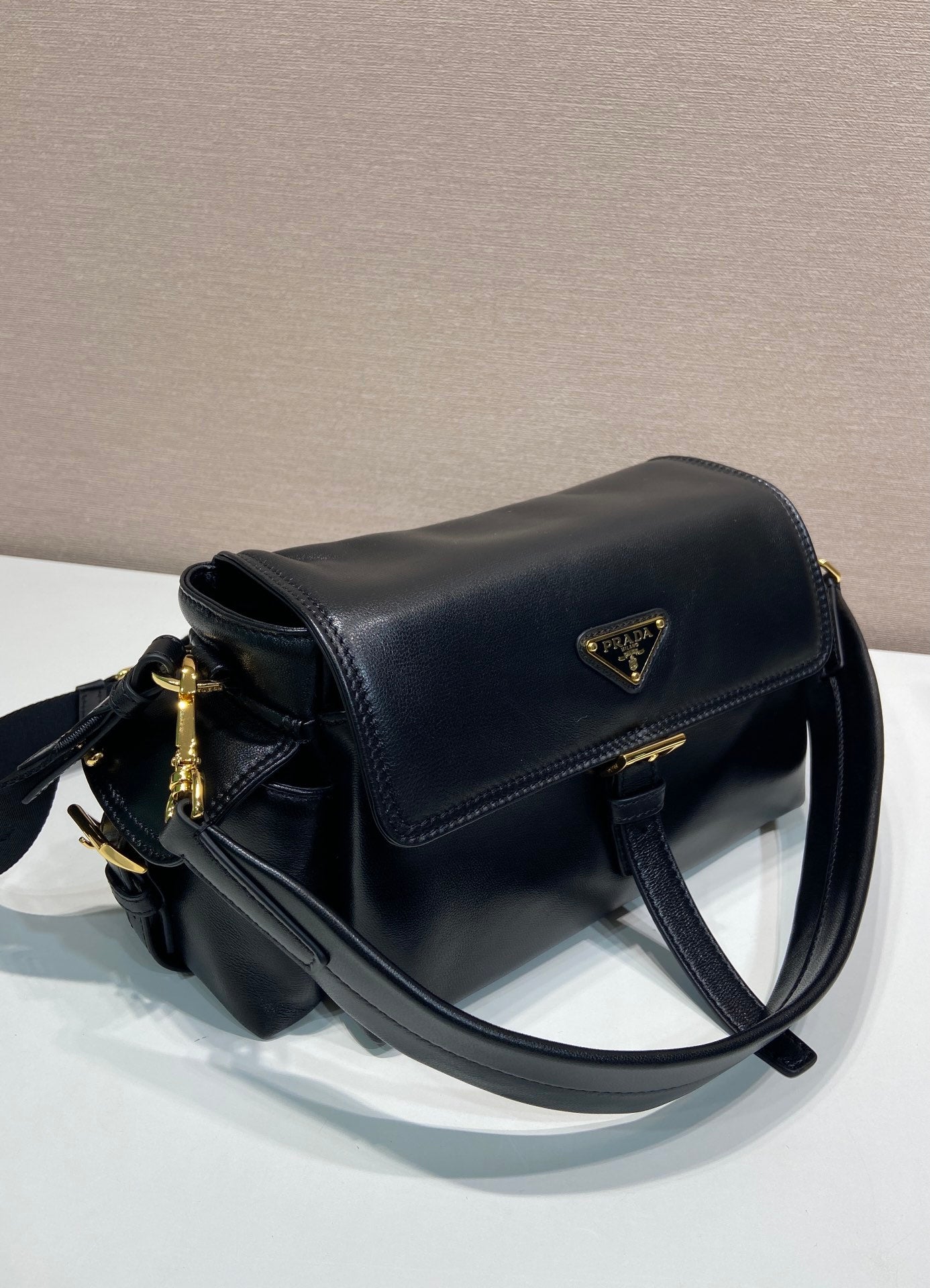 Prada black leather shoulder bag with curved flap, gold zipper pull, and side stitching.