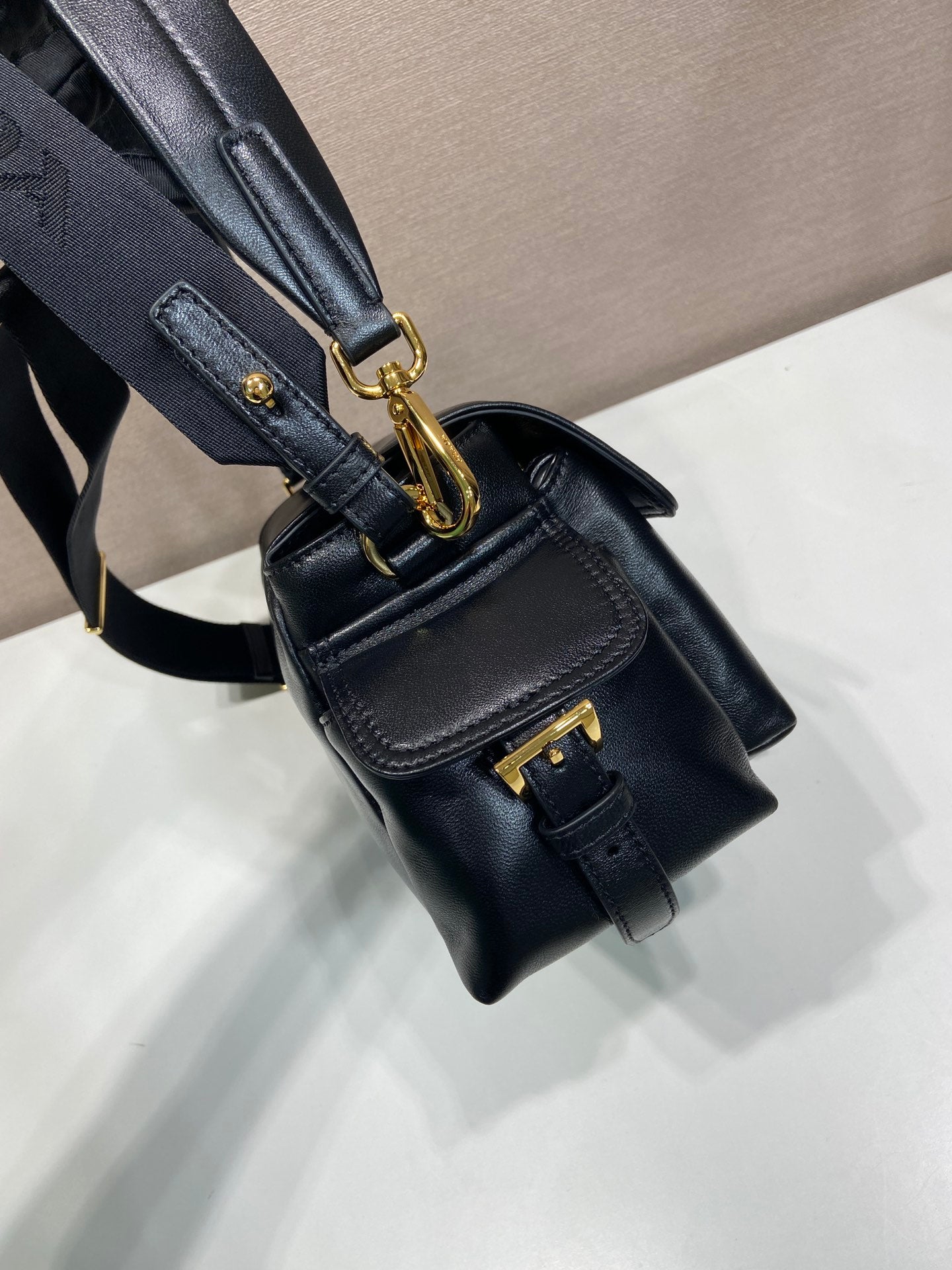 Prada black leather bag with gold clasp, crossbody strap, and flap pocket detail.