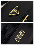 Prada logo plaque on black leather handbag with gold lettering and stitched trim.