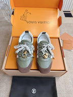 Low-top sneakers, olive and brown uppers, white laces with gold charm accents.