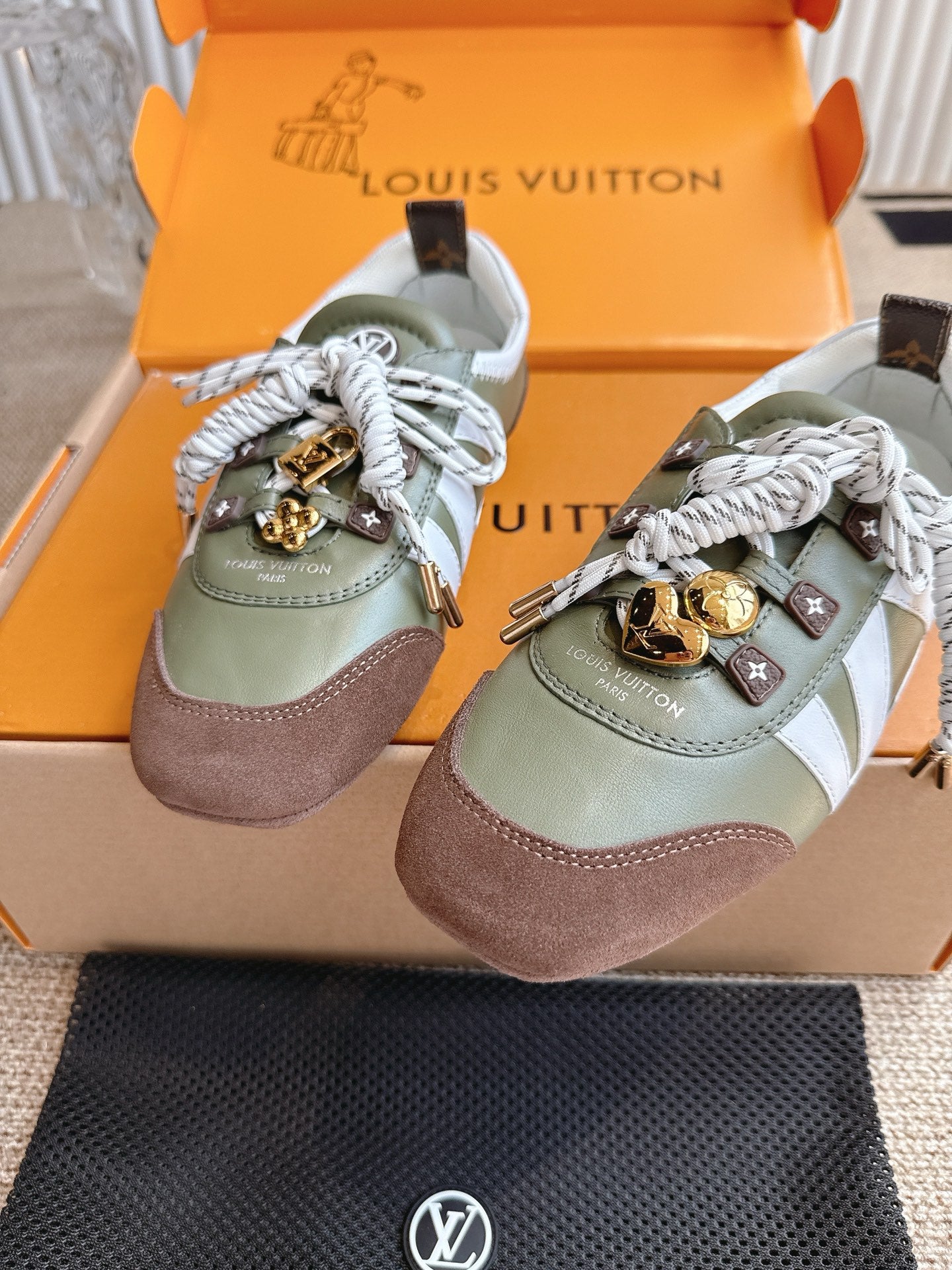 Pair low-top sneakers, olive and brown panels, white laces with gold and monogram charms.
