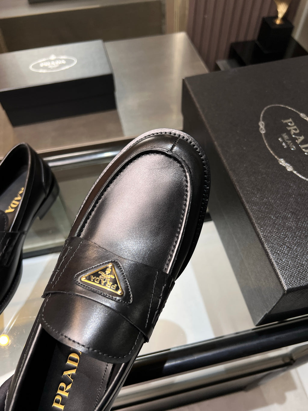Black leather loafer close-up with gold triangular logo and rounded toe