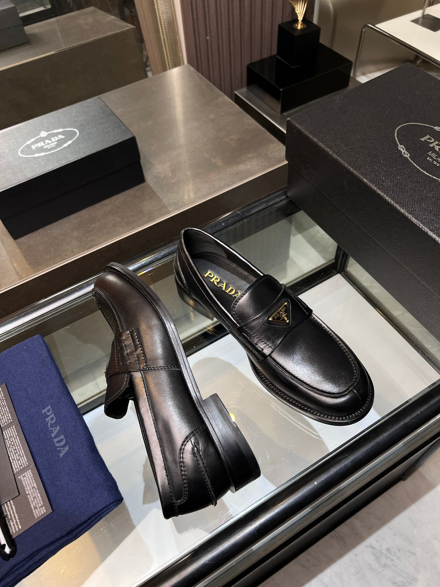 Black leather loafers displayed in a mirror case, slip-on style with logo