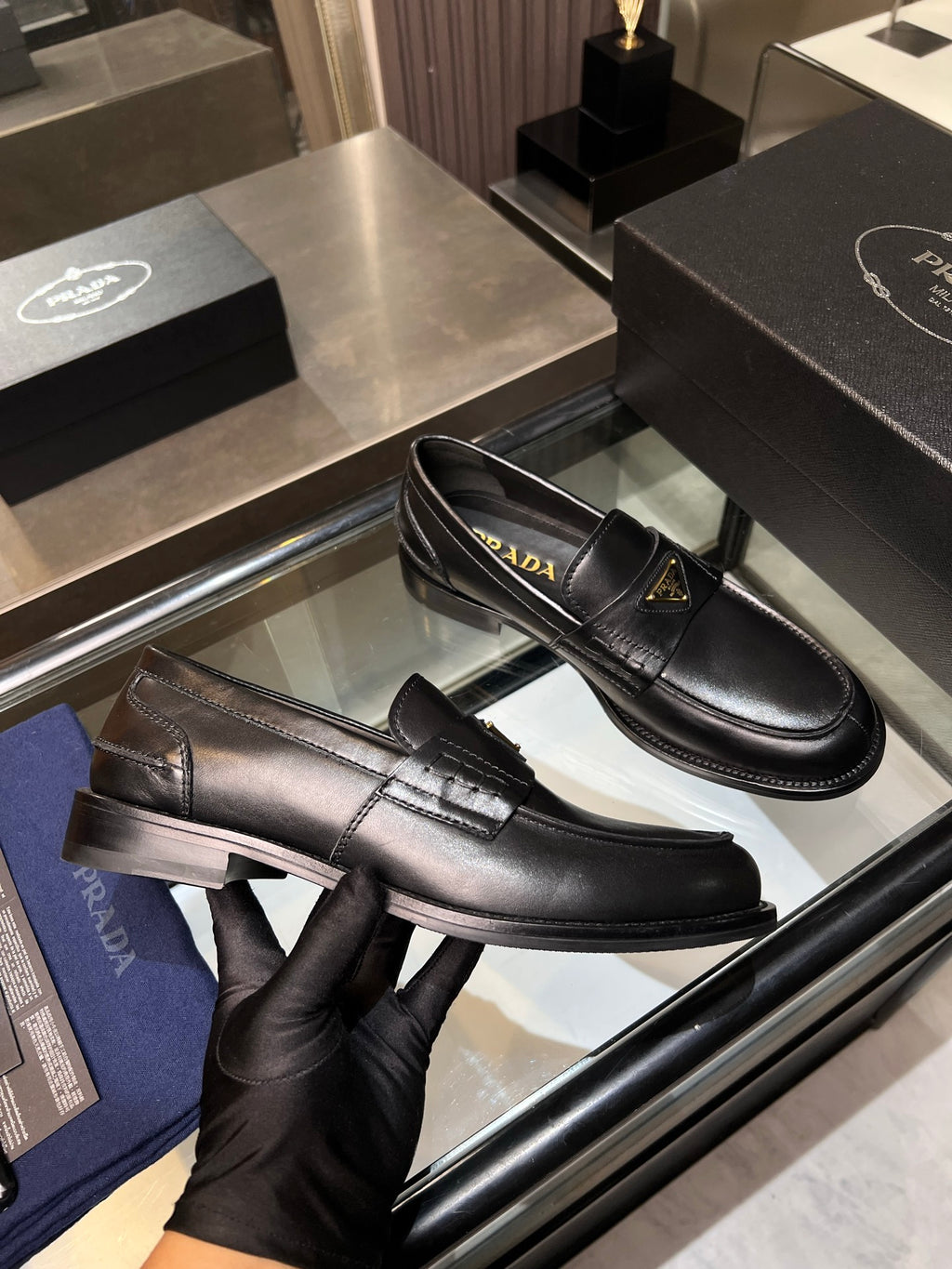 Black leather loafers with gold triangular logo; one pair shown side-by-side
