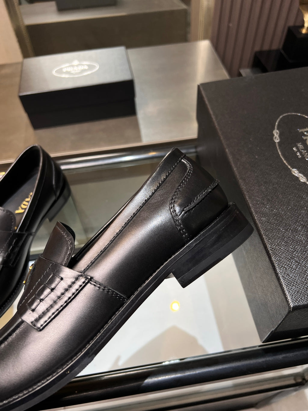 Black leather loafer with side stripe and stitched trim; gold triangular logo