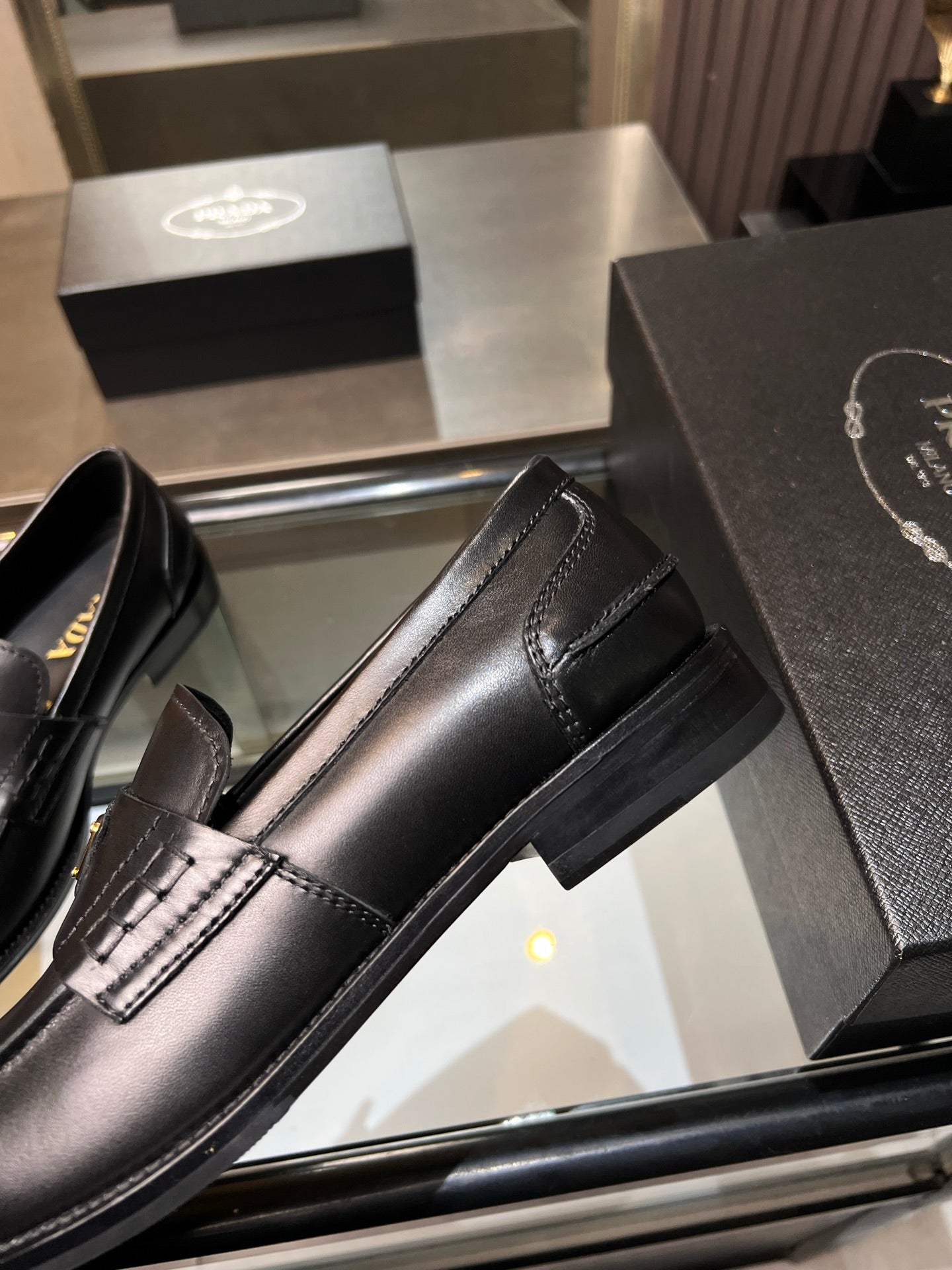 Black leather loafer with side stripe and stitched trim; gold triangular logo
