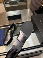 Black leather loafers shown from side with textured sole and logo vamp