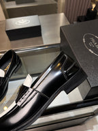 Black Prada penny-style loafer with glossy finish, stacked heel, stitched detail.