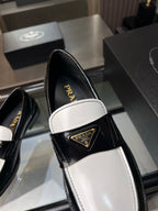 Prada loafer close-up: black upper, white trim, gold logo plaque on strap.