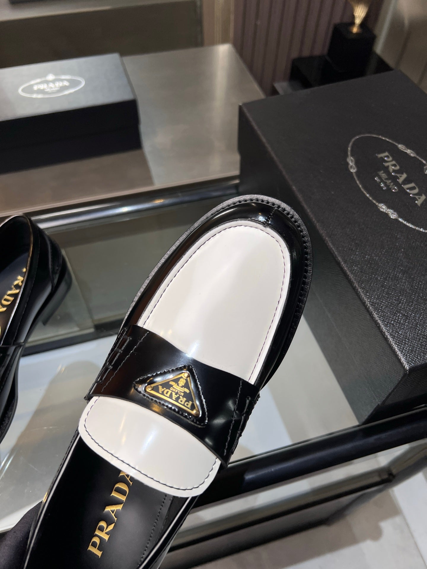 Prada loafer heel view with white insole, black upper and gold logo plaque.