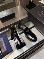 Black patent leather loafers set on display tray with stitched sole edge and Prada branding