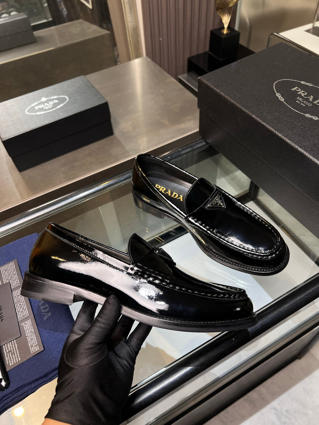 Black patent leather loafers with patterned strap accent and Prada logo on the side