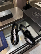 Black patent leather loafers with square toe, decorative strap, and Prada branding on uppers