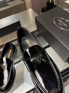 Black patent leather loafers with pointed square toe, strap ornament, and Prada label inside