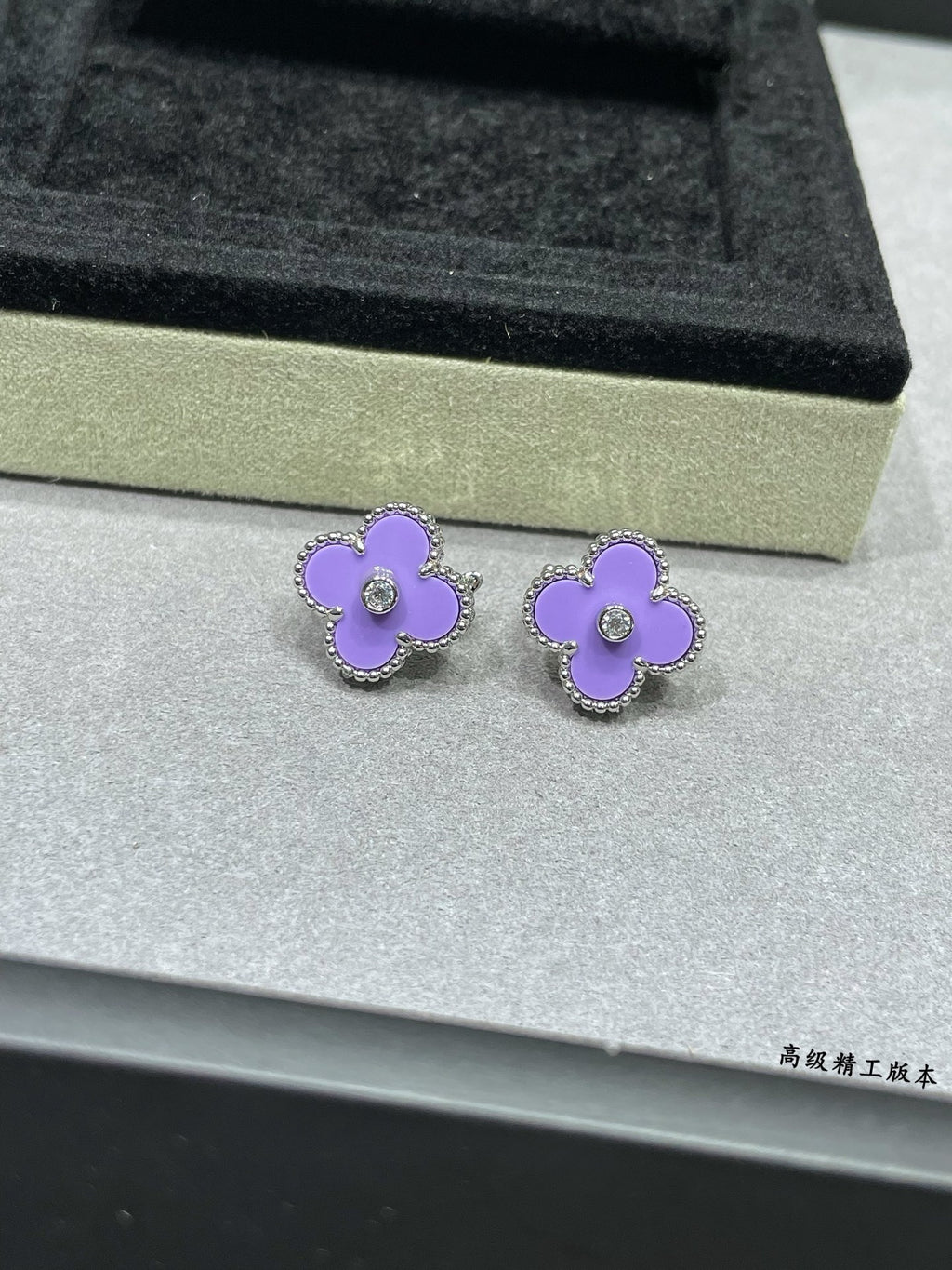 Lilac clover stud earrings resting on a jewelry box insert with clear center stones