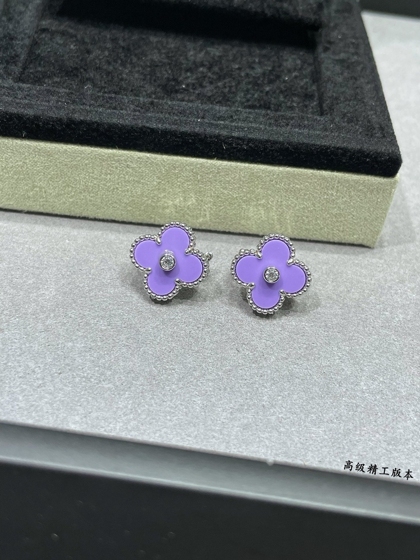 Lilac clover stud earrings resting on a jewelry box insert with clear center stones