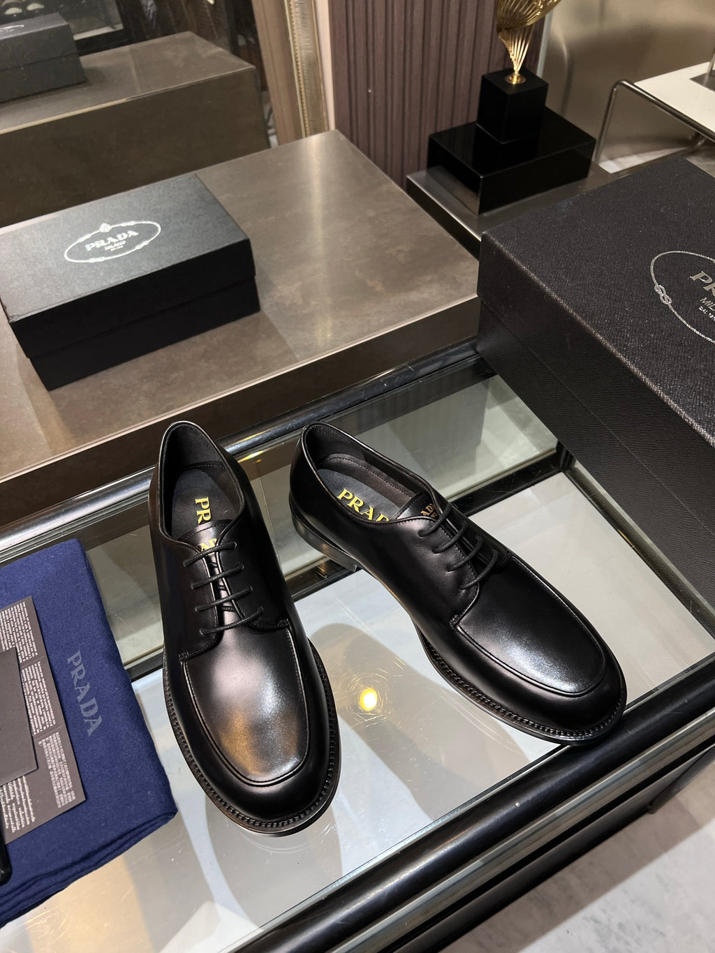 Black leather oxford shoes with lace-up closure, side view in display tray