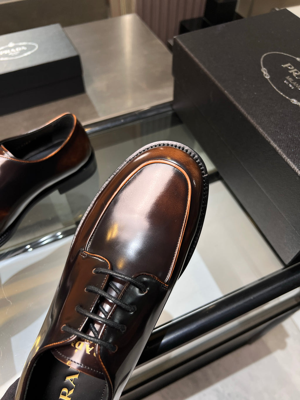 Angled view of dark brown lace-up oxford shoe with glossy finish and Prada logo