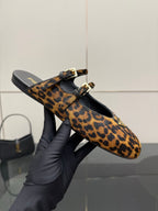 Prada leopard-print flats held in hand, showing strap and gold buckle