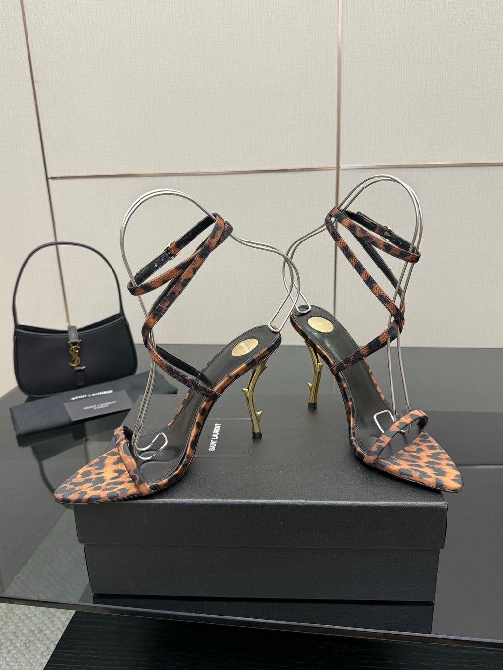 YSL women’s leopard-print heeled sandals with thin black ankle straps and gold-tone stiletto heels