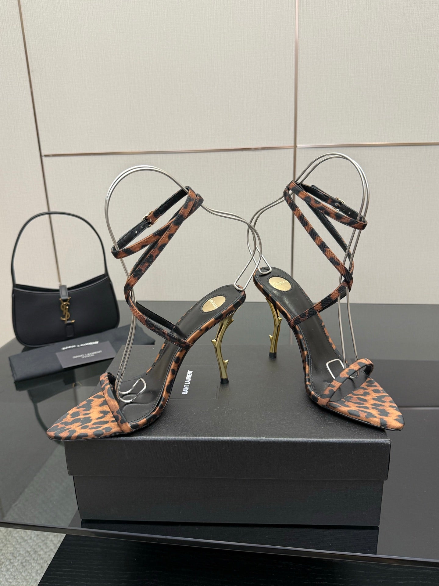 YSL women’s leopard-print heeled sandals with thin black ankle straps and gold-tone stiletto heels