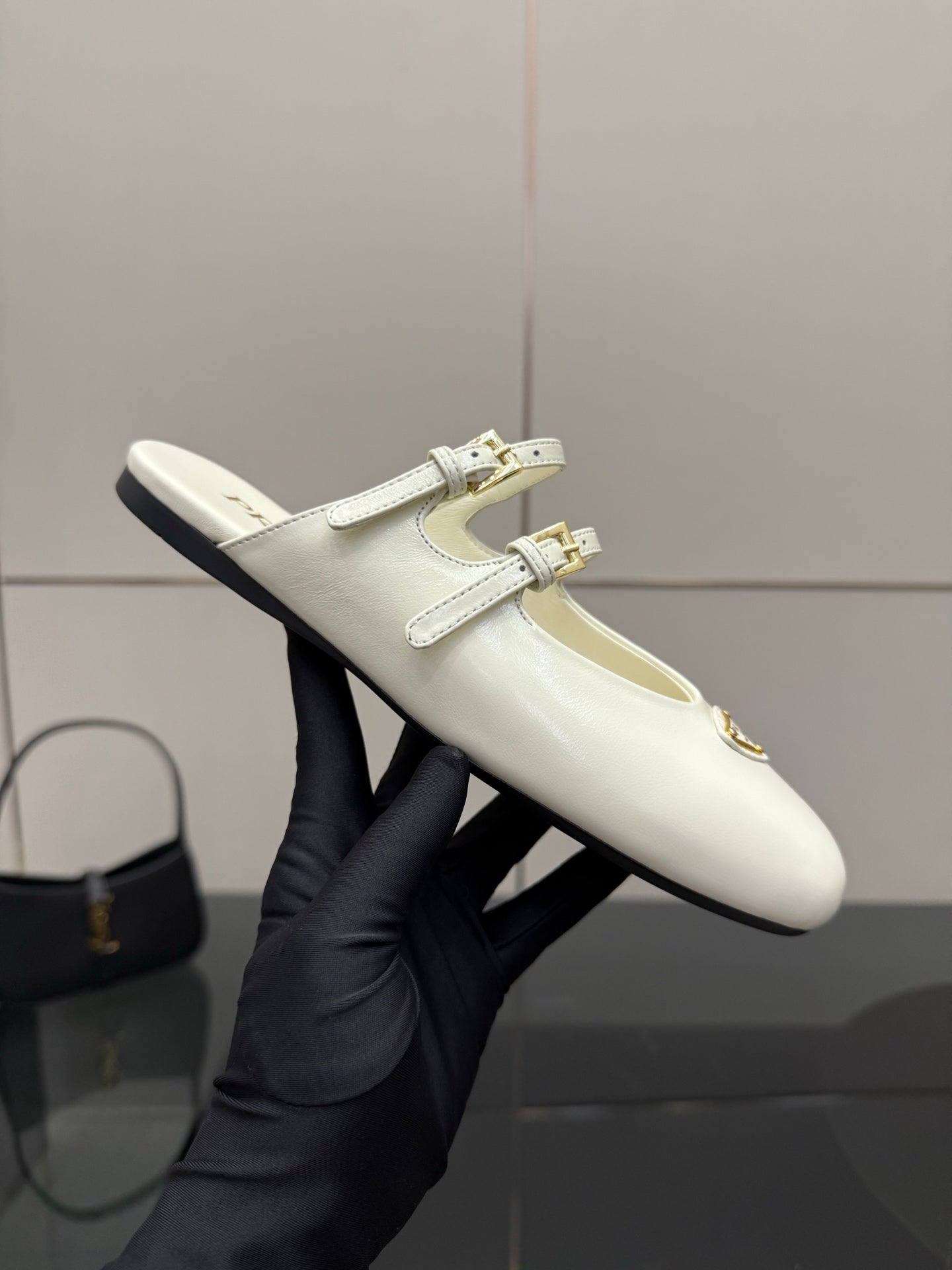 Women's Prada white leather flat shoe held up, double buckle strap and logo patch