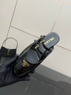 Women's black Prada slip-on shoe with gold buckle strap and logo footbed
