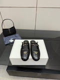 Women's black leather Prada slip-on shoes with gold buckle detail