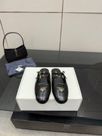 Women's black leather Prada slip-on shoes with gold buckle detail