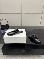Women's black leather Prada slip-on shoes with gold buckle hardware detail
