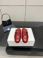 Red leather mule flats with decorative gold logo emblem and buckle strap