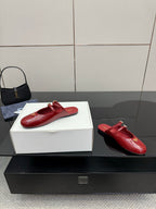 Red leather mule flats with gold buckle detail, side view on display box