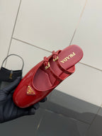 Red leather mule flats with gold buckle straps and circular logo emblem on insole