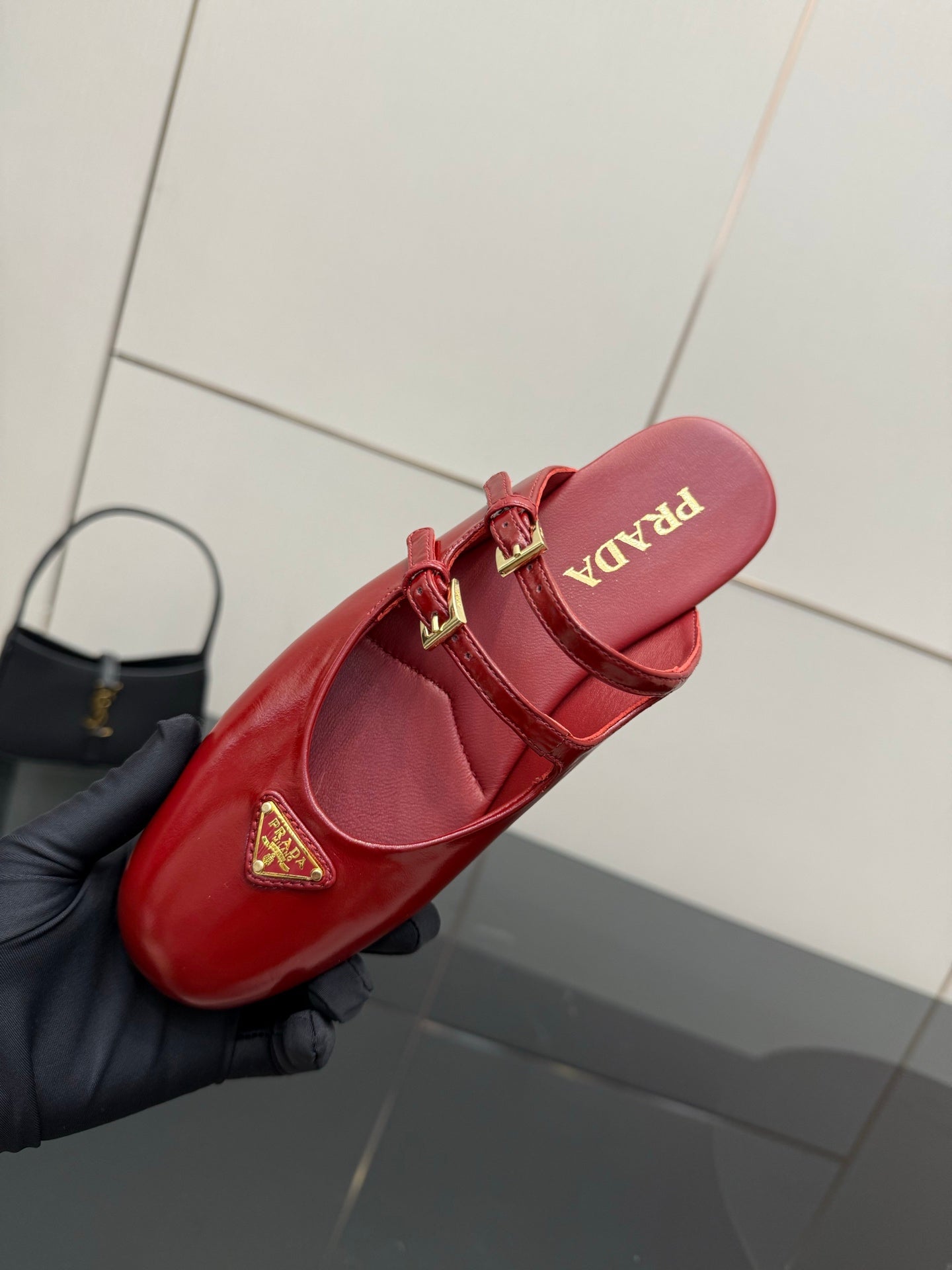 Red leather mule flats with gold buckle straps and circular logo emblem on insole