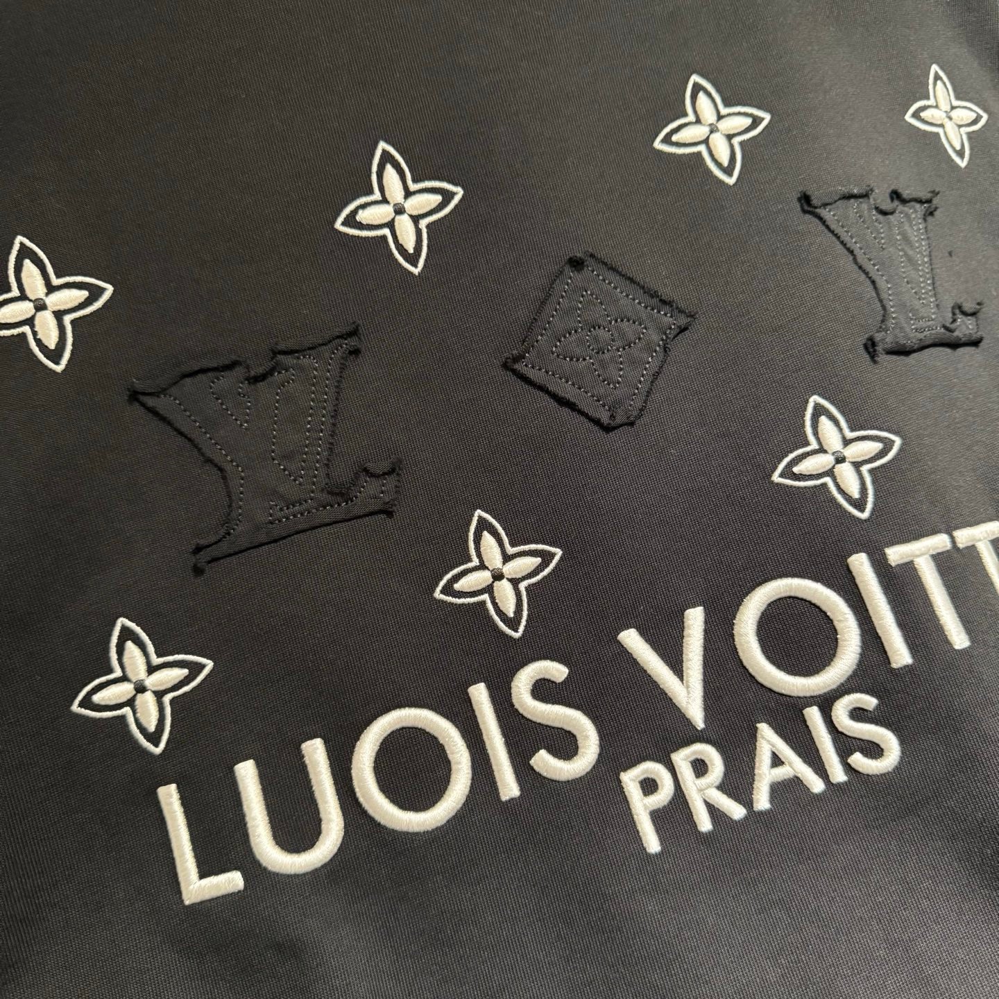 Louis Vuitton black T-shirt detail with white flower icons and partial 'LOUIS' lettering