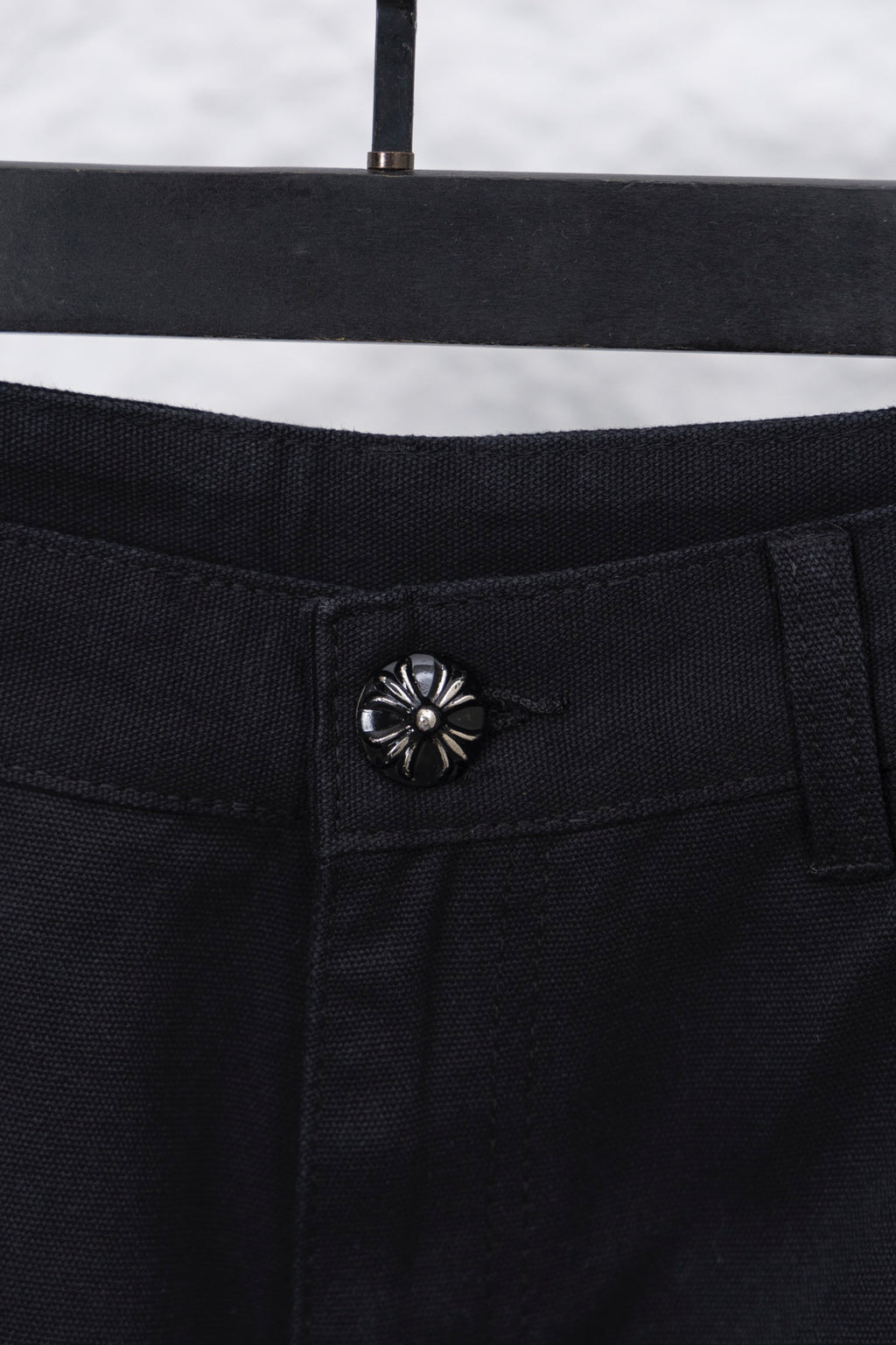 Black cargo pants waistband button closure with decorative flower-style rivet