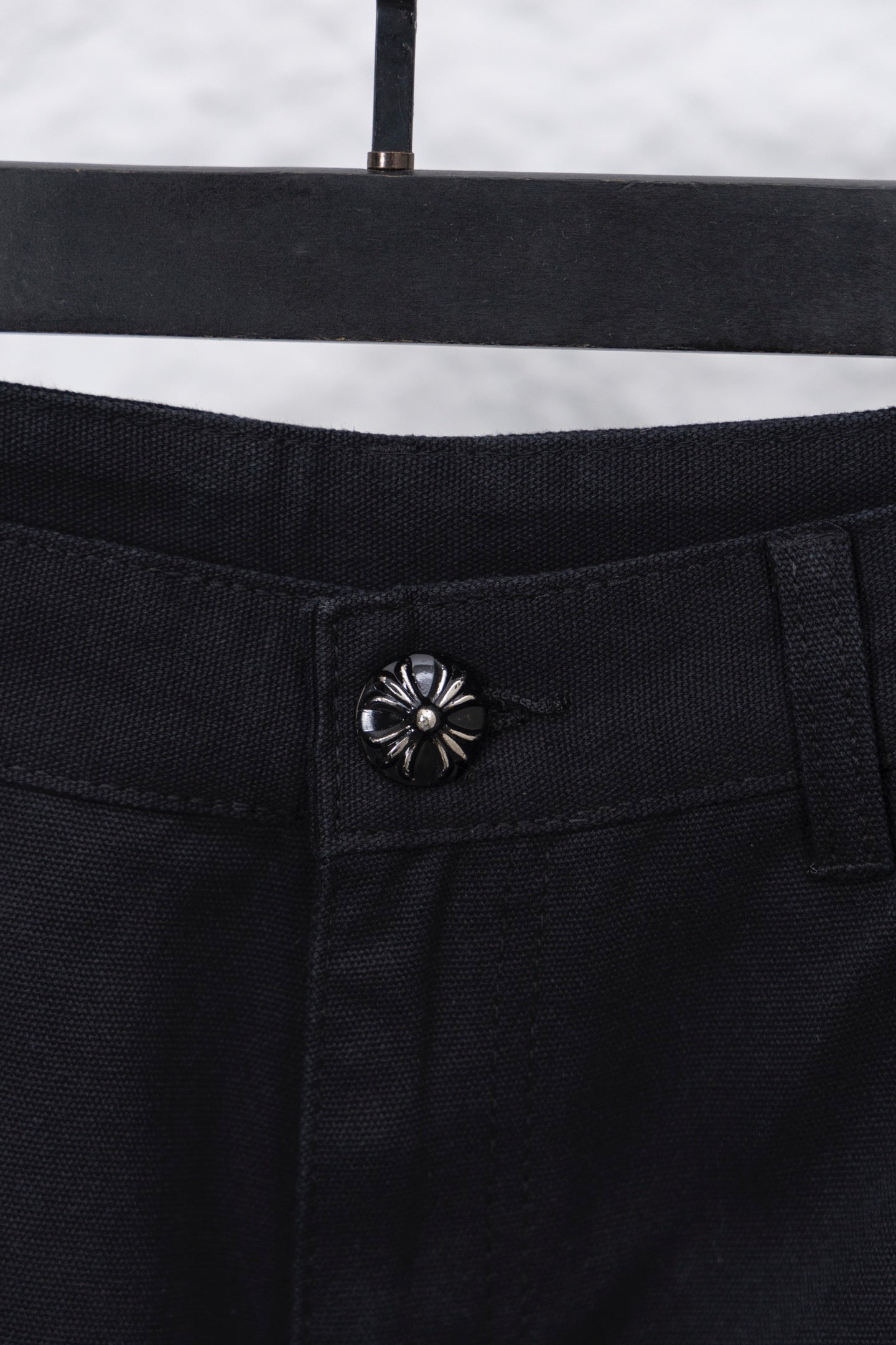 Black cargo pants waistband button closure with decorative flower-style rivet