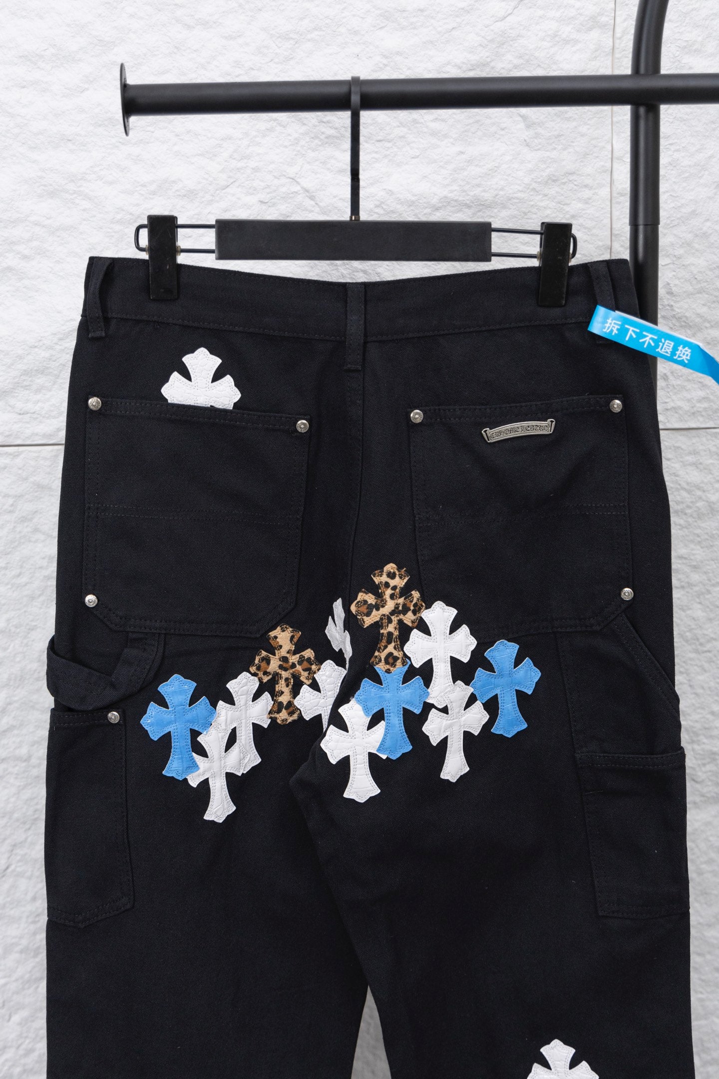 Black cargo pants with large front cross appliques in blue, white, and gold tone