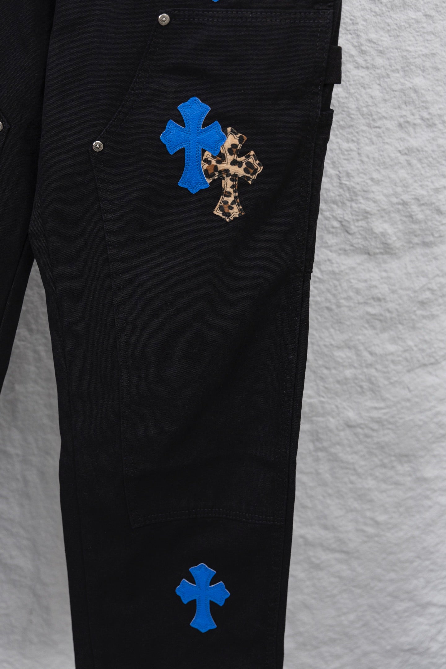 Black cargo pants side close-up with leopard-and-blue cross patch at thigh