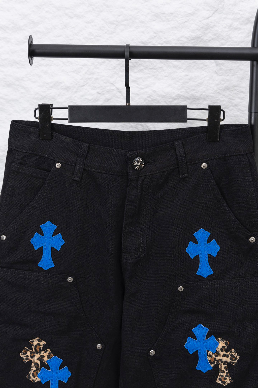 Black cargo pants front close-up with blue cross patches and decorative buttons