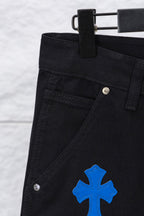 Black pants close-up: waistband button, angled seam, and blue cross patch