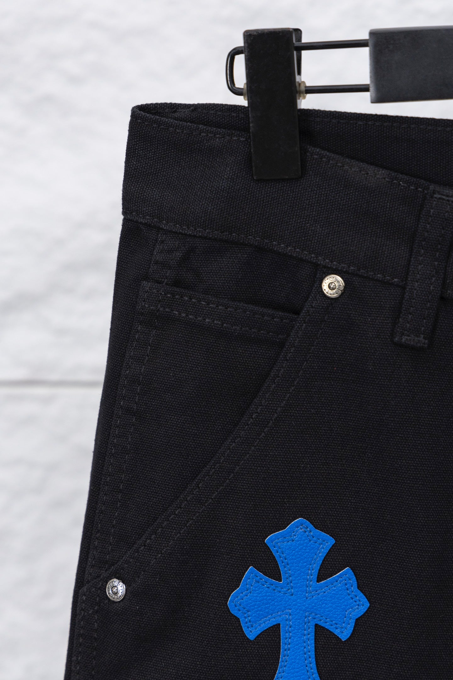 Black pants close-up: waistband button, angled seam, and blue cross patch
