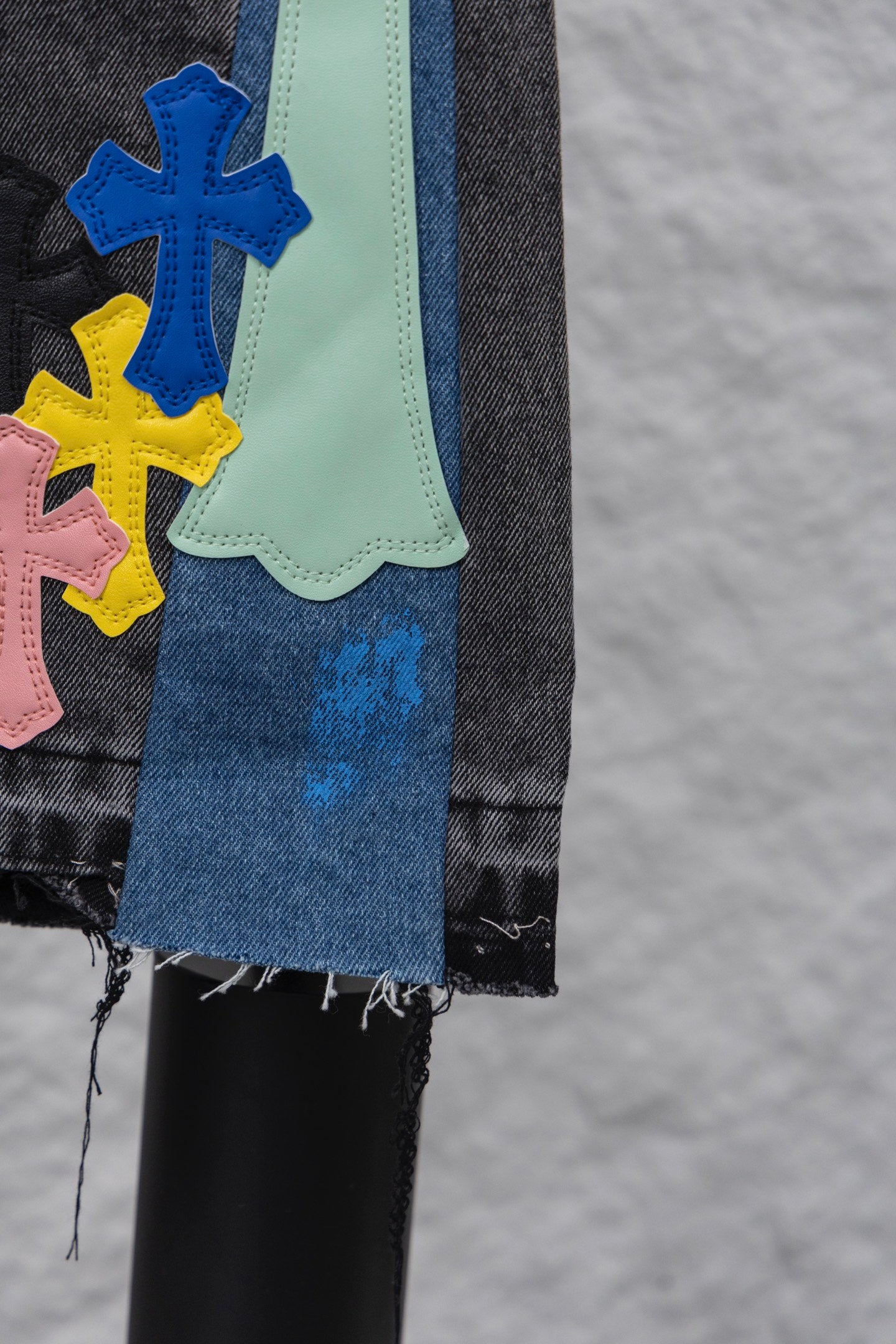 Denim pants with colorful cross patches and frayed hem, dark blue wash