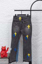 Dark denim pants with cross applique patches in yellow, blue, and black; front view.
