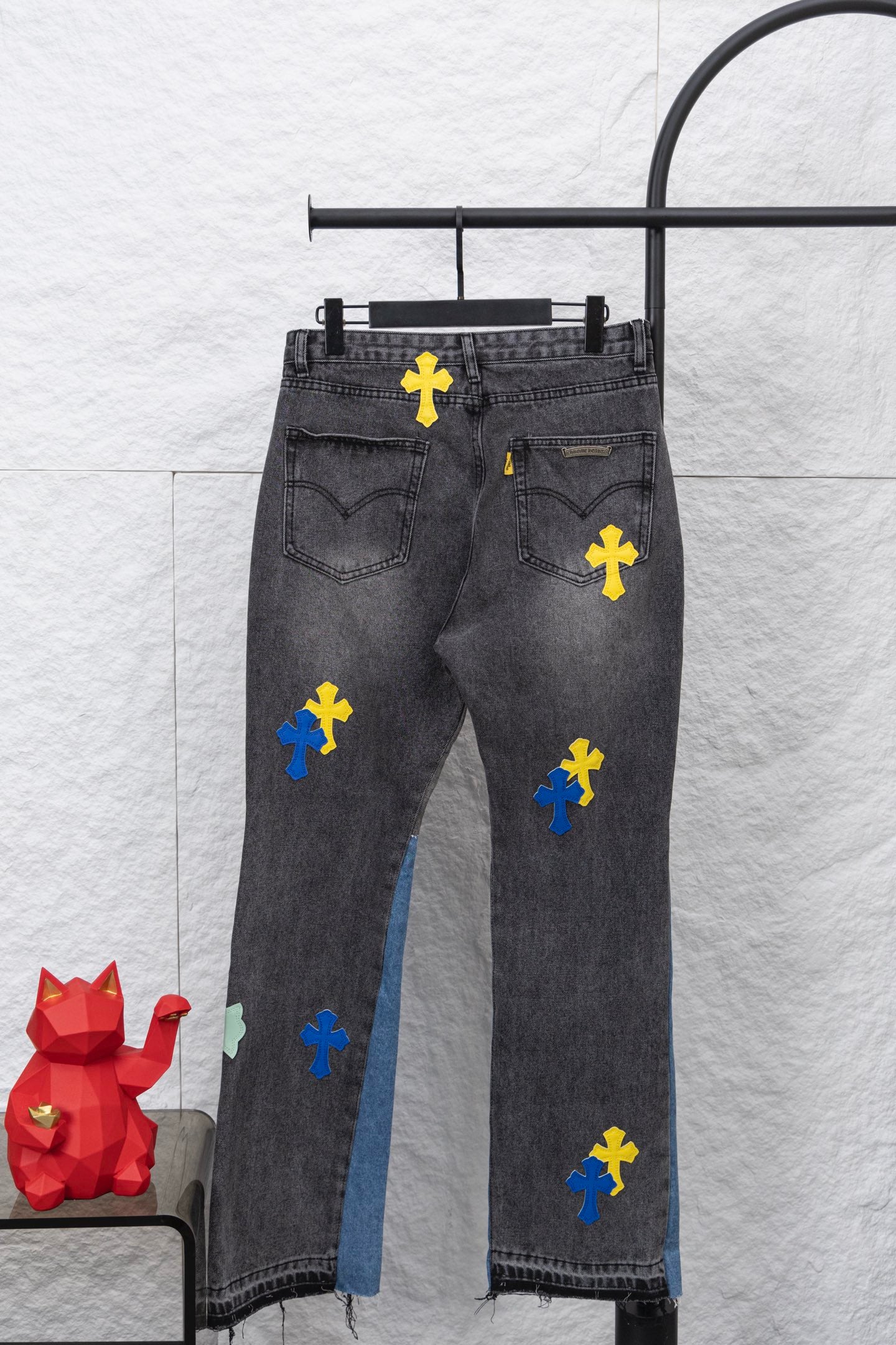 Dark denim pants with cross applique patches in yellow, blue, and black; front view.