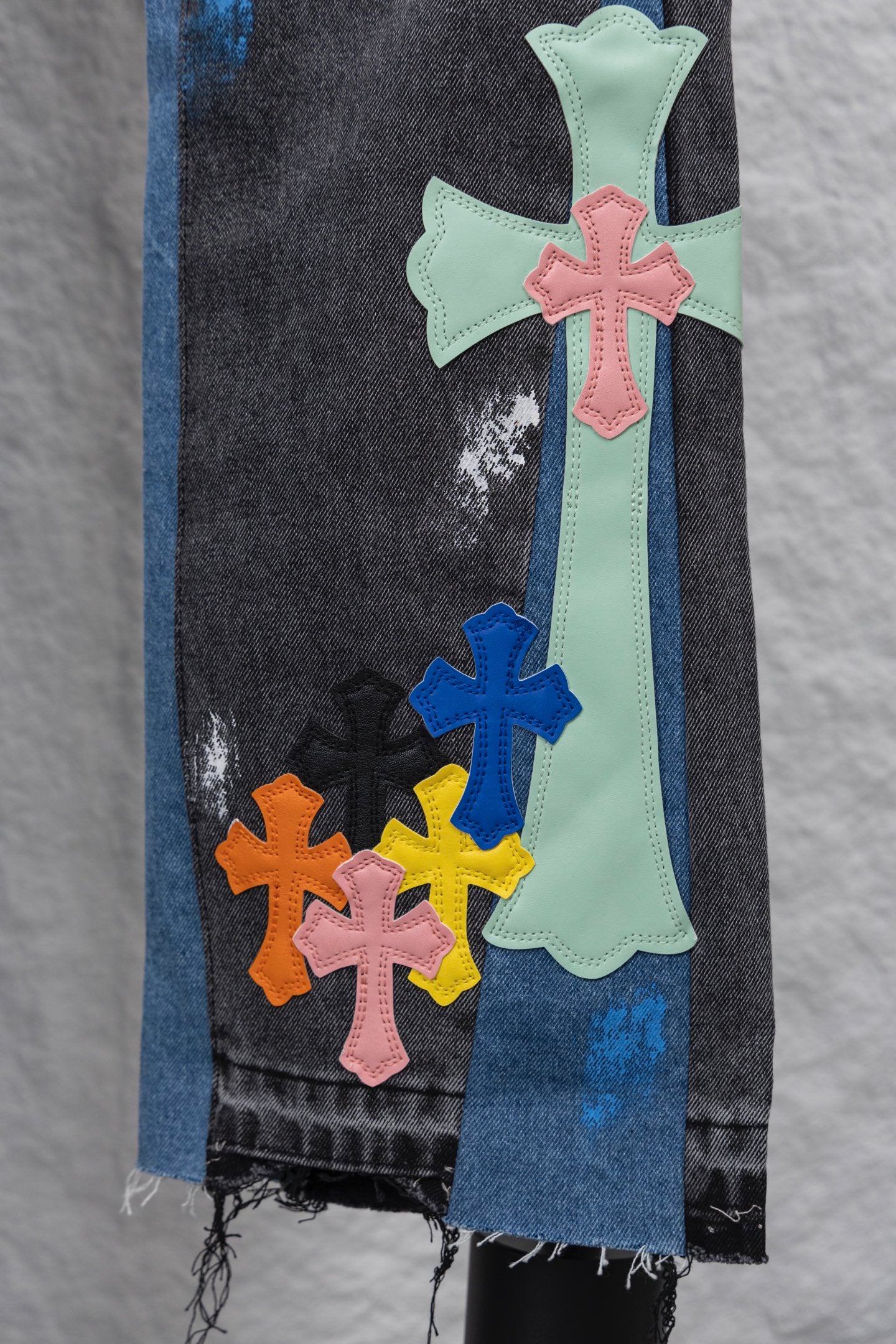 Black denim pants with large cross patches in mint, pink, blue, and orange; close-up.