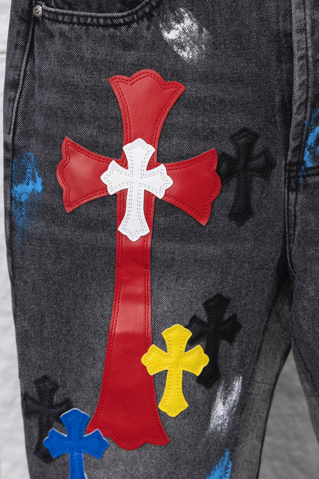 Close-up of red cross patch with white cross center on black denim pants; multicolor accents.