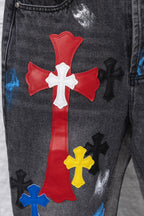 Close-up of red cross patch with white cross center on black denim pants; multicolor accents.