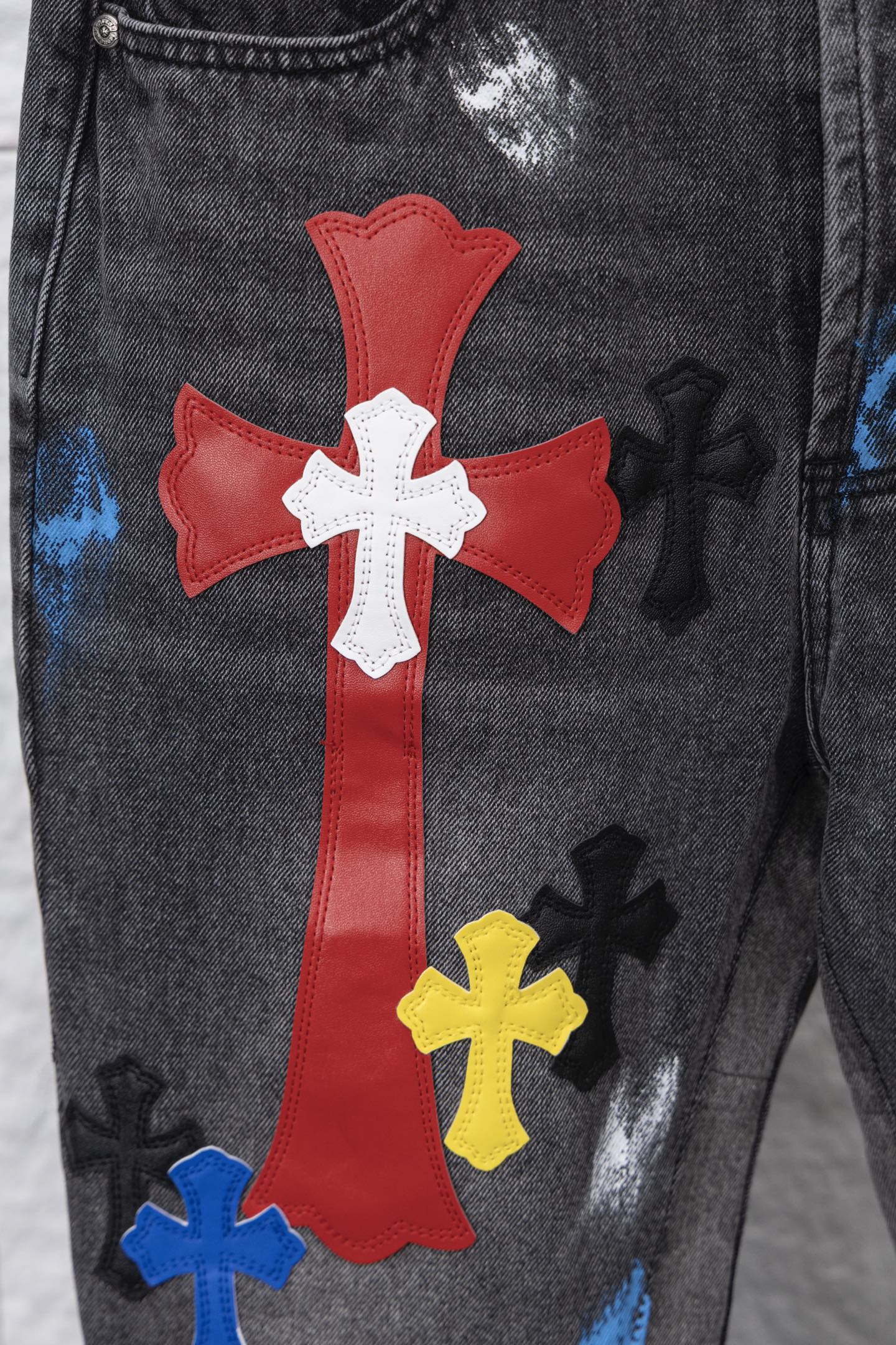 Close-up of red cross patch with white cross center on black denim pants; multicolor accents.
