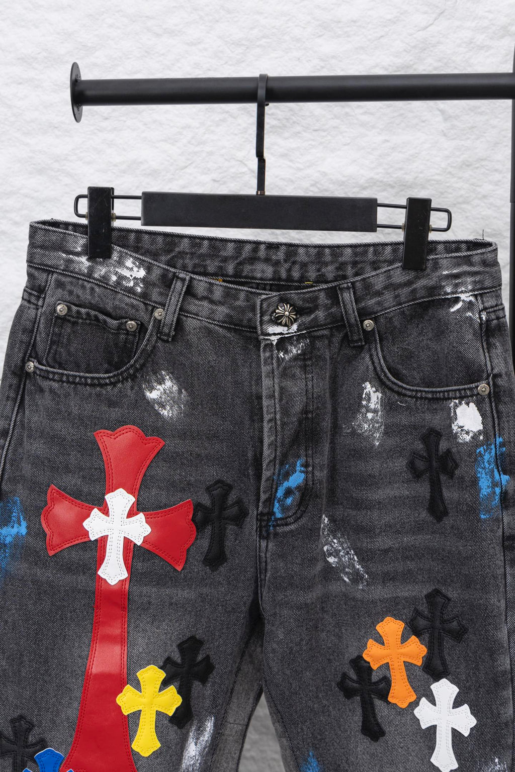 Black denim pants with large red cross patch and scattered multicolor cross appliques.